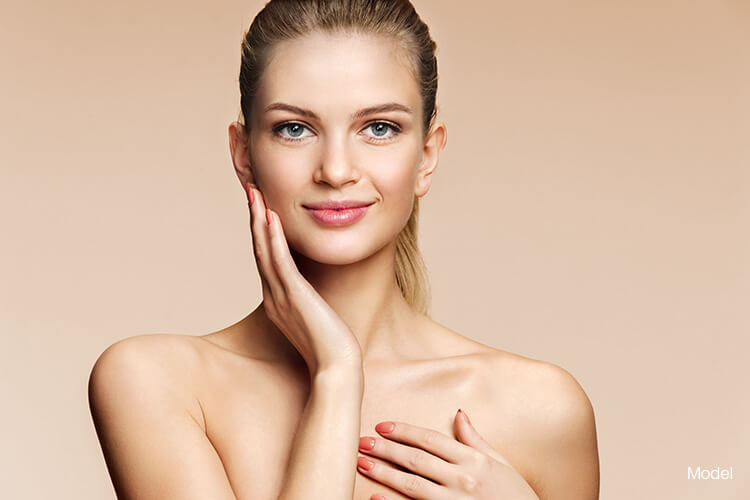 Young woman with one hand touching the side of her face and the other hand resting on her upper chest.