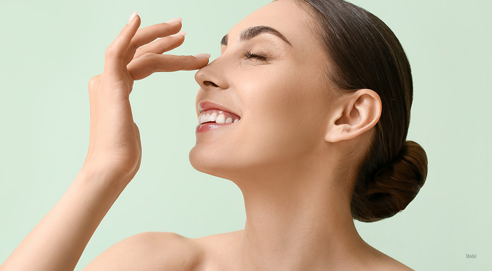 Smiling young woman with her hair in a bun touching her nose on a color background.