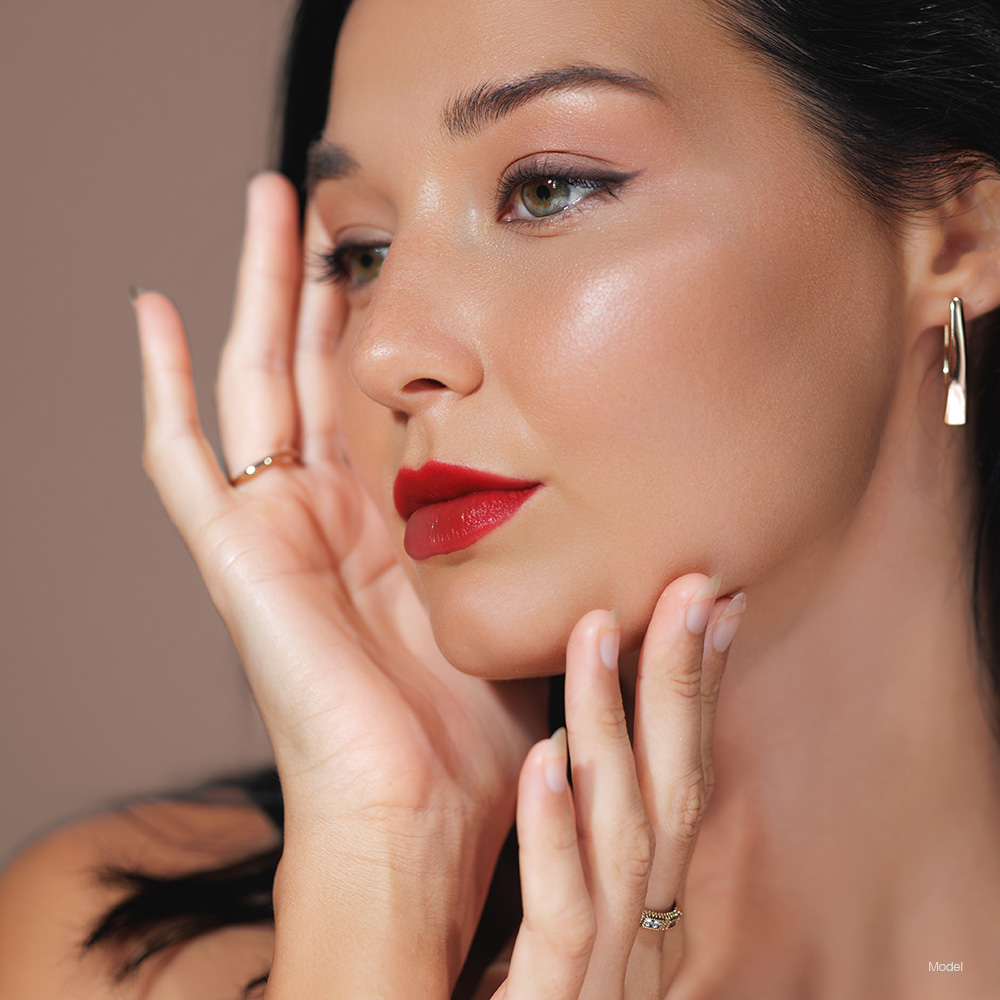 Young woman with red lipstick touching her face
